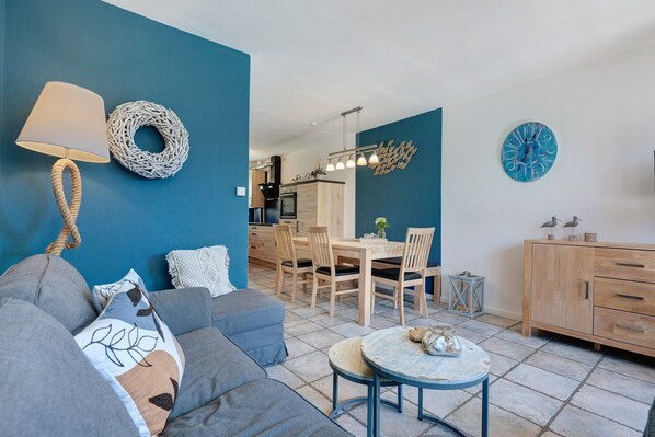 A modern living room with a sofa, a round coffee table, and a dining area with wooden chairs and a table.