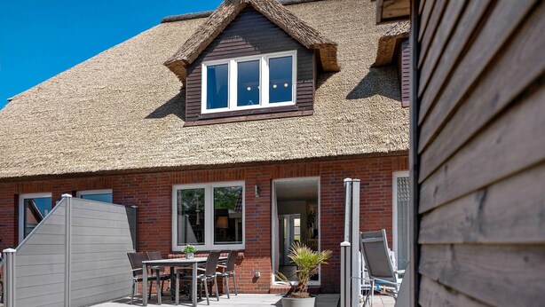 A house with a thatched roof, a brick exterior, and a patio with outdoor furniture. - Düün Drööm – Your Dream House Behind the Dunes (St. Peter-Ording Dorf)