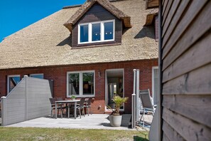 A house with a thatched roof, a brick exterior, and a patio with outdoor furniture.