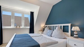 A bedroom with a bed, nightstands, a lamp, and a window with curtains. - Düün Drööm – Your Dream House Behind the Dunes (St. Peter-Ording Dorf)