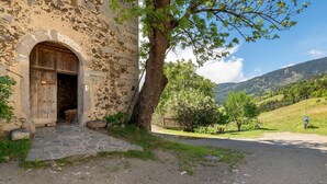 A stone building with an arched entrance, a tree in front, and a rural landscape with hills in the background. - Apartment 'Gravetsch Kloster Säben' with Mountain View, Shared Garden and Wi-Fi (Villandro)
