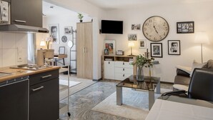 A modern kitchen with a built-in oven, a dining area with a glass table, and a living space with a sofa and a TV mounted on the wall. - Studio 'Moonraker' with Shared Terrace and Wi-Fi (Breisach am Rhein)