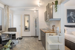 Een kleine hotelkamer met een kitchenette, een eethoek, een spiegel en een bed.
