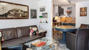 Ein Wohnzimmer mit einem braunen Ledersofa, einem Glastisch mit einem Schachspiel und einem Essbereich mit blauem Tisch und Stühlen.