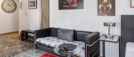 A modern living room with a sofa, a glass coffee table, a side table, a clock, and wall art.