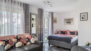A modern hotel room with a bed, sofa, and a dining area.