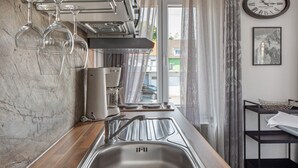 A modern kitchen with a stainless steel sink, hanging wine glasses, and a clock on the wall.
