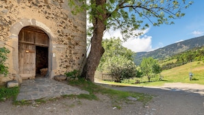 A stone building with an arched entrance, a tree in front, and a rural landscape with hills in the background. - Apartment 'Schloss Gravetsch Castel' with Mountain View and Shared Garden (Villandro)