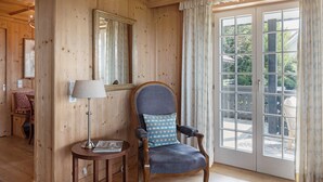 A wooden-paneled room with a large window, a chair with a patterned cushion, a lamp, and a mirror on the wall.