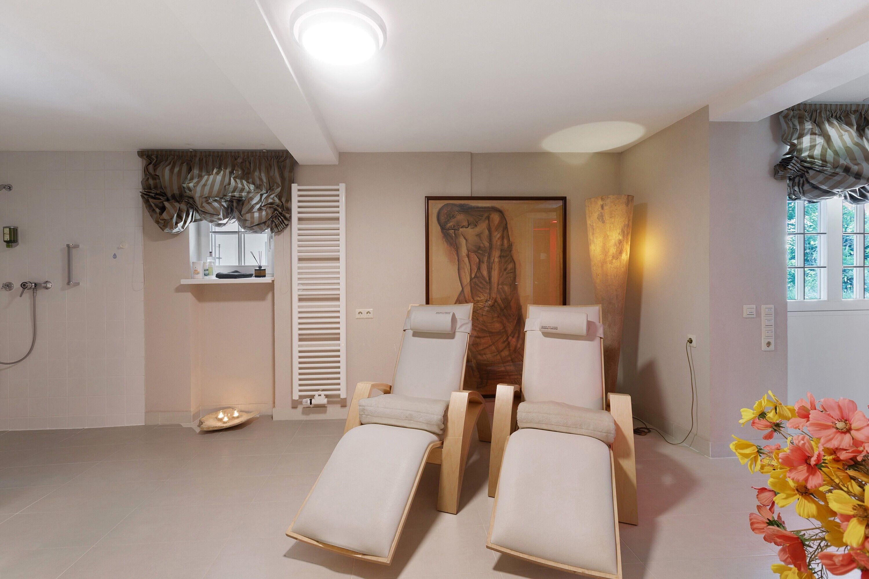 A room with two reclining chairs, a large painting, a window with curtains, and a shower area.