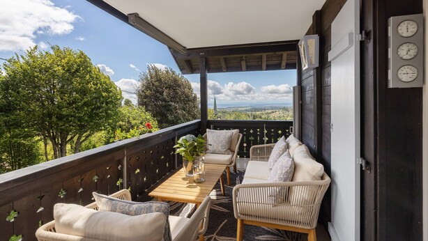 A balcony with outdoor furniture, a table with a vase, and a view of trees and mountains.