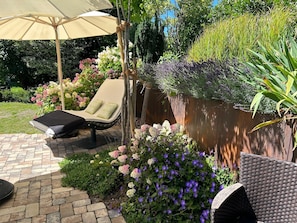 Un patio con una poltrona da relax, un ombrellone grande e diverse piante fiorite.