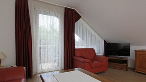A room with a red sofa, a white rug, a television on a wooden stand, and a large window with curtains.