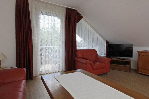 A room with a red sofa, a white rug, a television on a wooden stand, and a large window with curtains.
