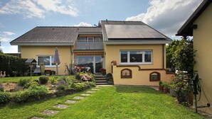 A two-story house with a garden, a solar panel on the roof, and a water pump.