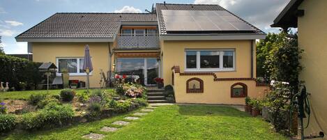 Ein zweistöckiges Haus mit Garten, einer Solaranlage auf dem Dach und einer Wasserpumpe.