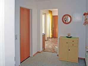 Um corredor com porta de madeira, um armário com gavetas e um espelho fixado na parede.