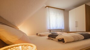 Un dormitorio con cama, mesita de noche, radiador y ventana con cortinas.