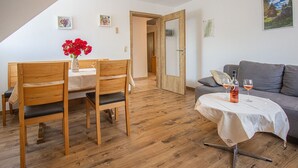 Una habitación con una mesa de comedor, sillas, un sofá, una mesita con bebidas y una puerta que da a otra estancia.