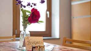 Une table sur laquelle se trouve un vase en verre contenant des fleurs, une carte avec le mot « BENVENUTI » et deux petits pots.