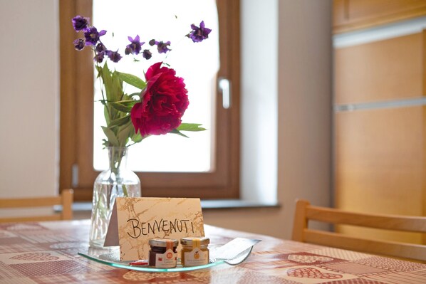 A table with a glass vase containing flowers, a card with 'BENVENUTI' text, and two small jars.