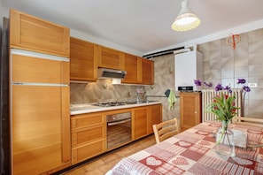 A kitchen with wooden cabinets, a stove, and a dining table with a patterned tablecloth.