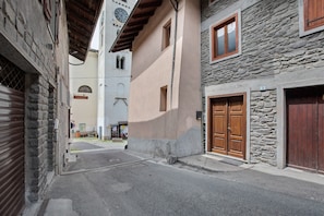 Une rue étroite bordée d’immeubles en pierre, de portes en bois et d’un beffroi bien visible.