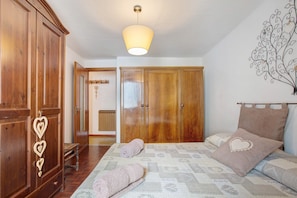A bedroom with a bed, wooden wardrobe, and a hanging light fixture.