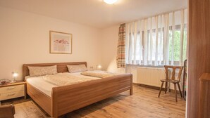 Een slaapkamer met een tweepersoonsbed, nachtkastjes, een stoel, een radiator en een raam met gordijnen.