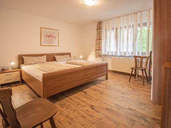 A bedroom with a double bed, bedside tables, a chair, a radiator, and a window with curtains.