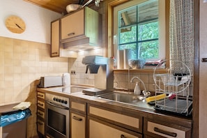 A kitchen with a stove, oven, sink, and a window with a view of greenery. - Sägerhäusle Holiday Home – Cozy Black Forest Cabin near Feldberg (Feldberg)
