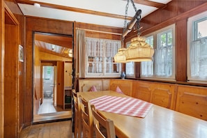A wooden interior with a dining table, chairs, a hanging light fixture, and a view through a door to a bathroom. - Sägerhäusle Holiday Home – Cozy Black Forest Cabin near Feldberg (Feldberg)