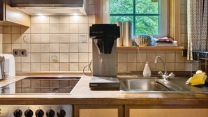A kitchen with a coffee maker, a sink, and a window with a view of greenery. - Sägerhäusle Holiday Home – Rustic Black Forest Cabin at Feldberg (Feldberg)