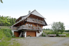 Ein mehrstöckiges Holzchalet mit Balkon, Garage und einer Treppe, die zum Obergeschoss führt.