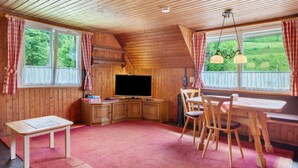 A cozy cabin interior with wooden walls, a flat-screen TV, a dining table with chairs, and large windows with curtains. - Holiday Apartment 'Mühle' – Cozy Getaway at Feldberg (Feldberg)