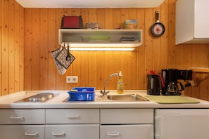 Une cuisine avec des murs en bois, un plan de travail blanc, un évier, une machine à café et une horloge.