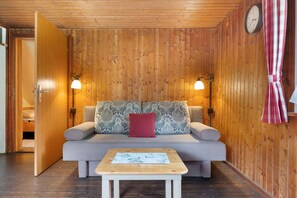 Une pièce aux murs lambrés, avec un canapé, une petite table et deux lampes fixées au mur.