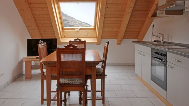 Ein Essbereich mit Holztisch und Stühlen, einem Fernseher und einer Küche mit Fenster und Blick ins Freie.