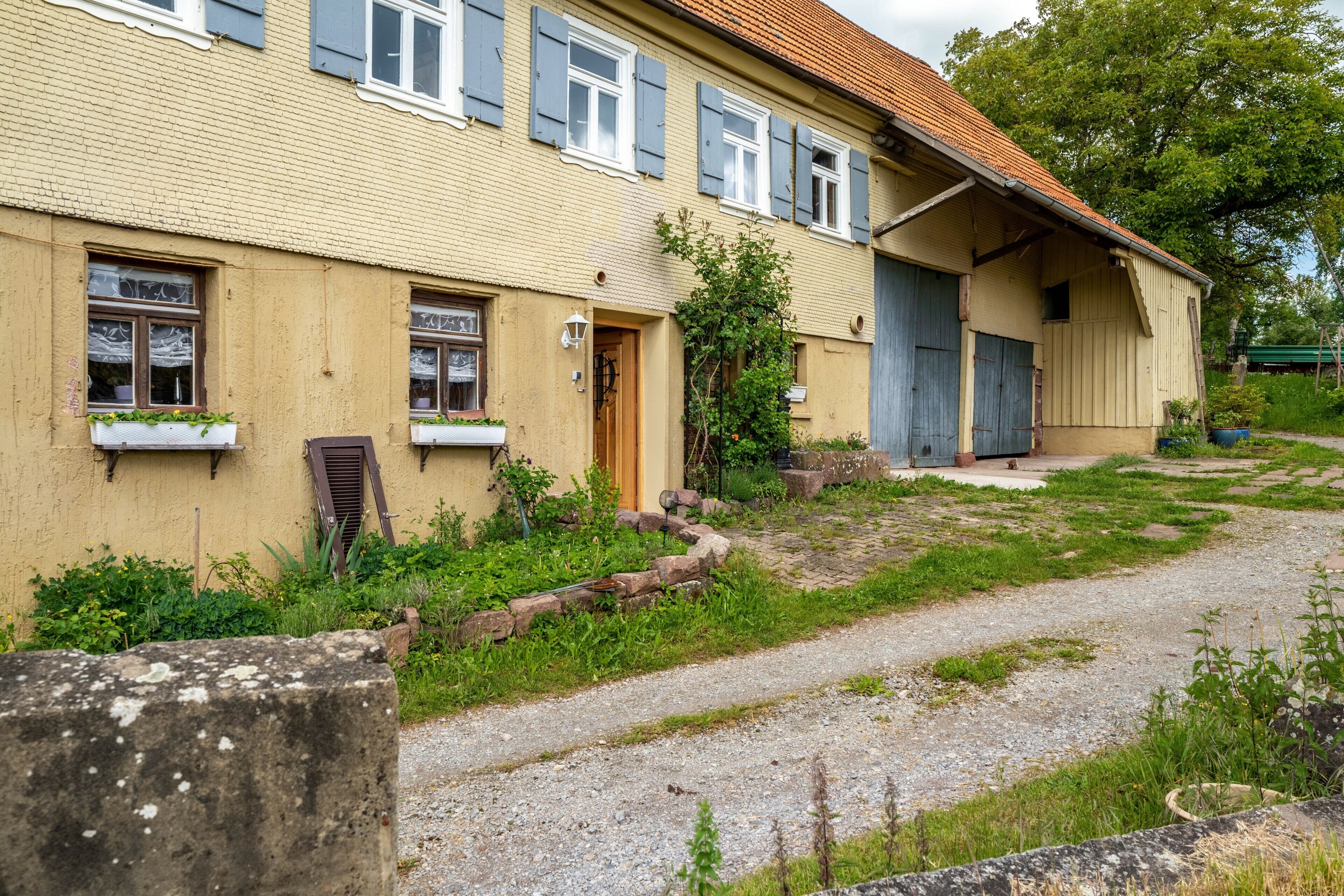 A two-story building with a yellow facade, multiple windows with shutters, and a gravel driveway.