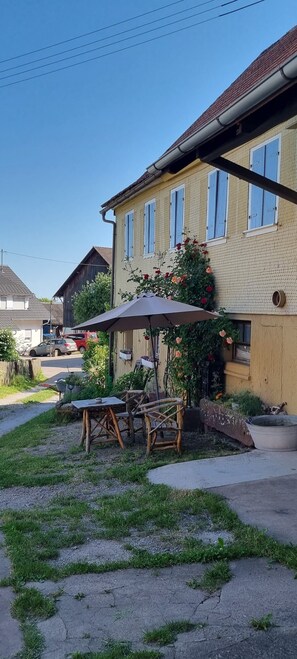 A residential area with a house featuring a brick facade, a wooden deck, and a garden with a table and chairs. - Studio 'Schwarzwald Ruhe' with Open Terrace in a Family-Friendly Setting (Altensteig)