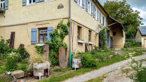 Un bâtiment à la façade en briques, doté de nombreuses fenêtres avec volets et d’un chemin de gravier menant à l’entrée.