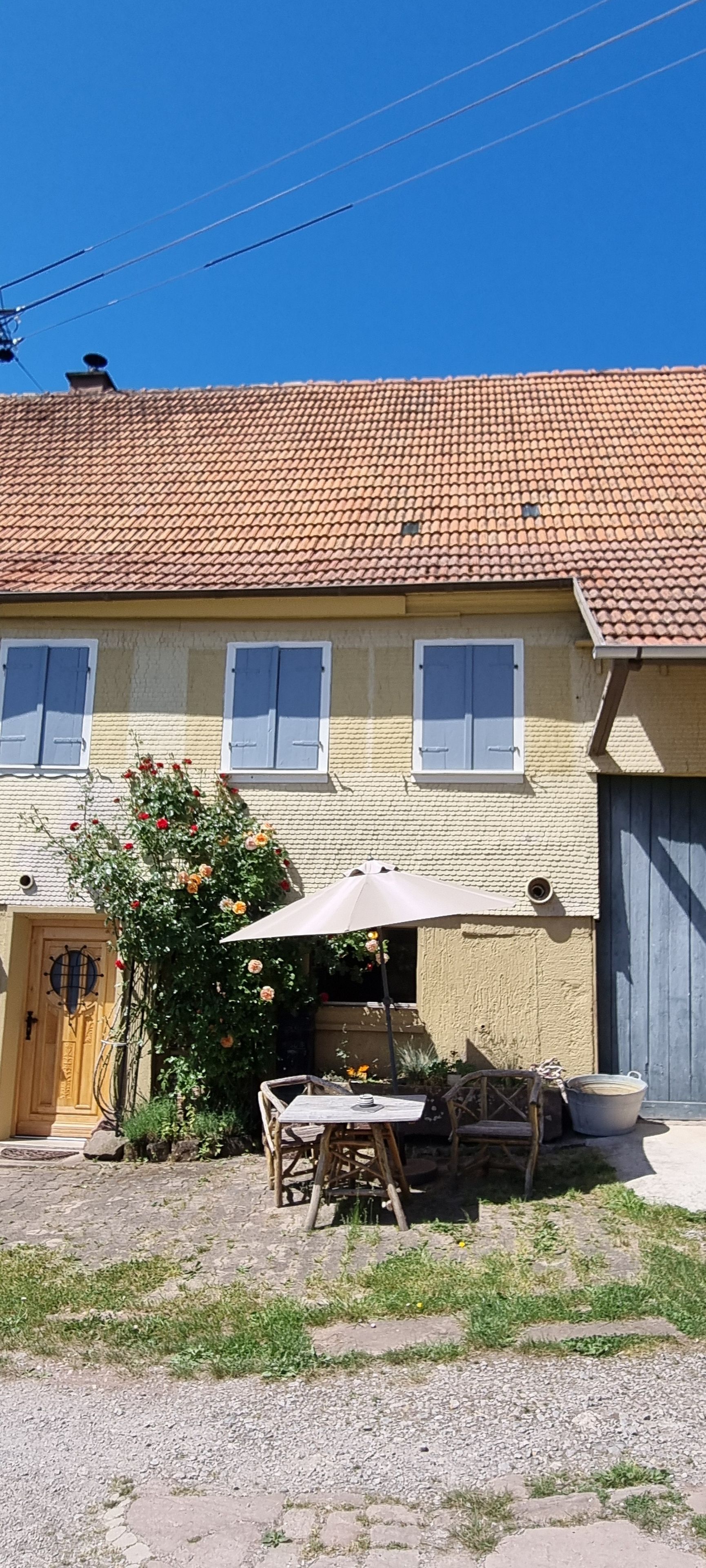 Une maison à deux étages, avec un toit en tuiles, une porte d’entrée et un petit patio aménagé avec du mobilier d’extérieur.