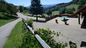 Un patio dallé avec des sièges extérieurs, un grand arbre et une vue sur une chaîne de montagnes.