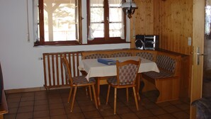 Une pièce avec un banc en bois, une table avec des chaises, un radiateur et une fenêtre avec des rideaux.