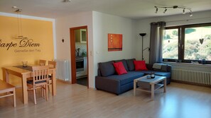Un salon moderne avec un canapé, une table à manger, des chaises et une cuisine en arrière-plan.