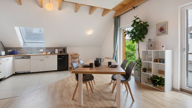 Een moderne keuken met houten balken, een eettafel met stoelen, een inbouwkast en een groot raam met uitzicht op groen.