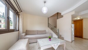 A living room with a sofa, a glass coffee table with a plant, a staircase, and a door.