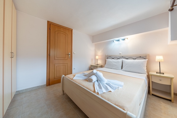A hotel room with a bed, wooden door, nightstands, and a lamp.