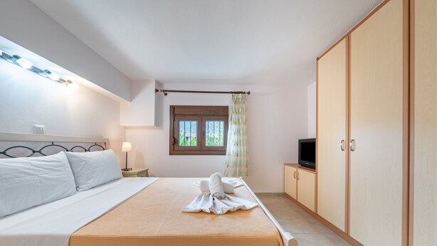 A bedroom with a bed, a TV, a wardrobe, and a window with curtains.