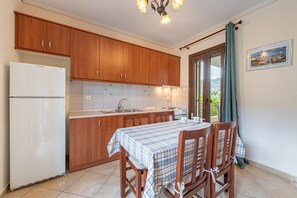 Een keuken met houten kastjes, een Bosch koelkast, een betegelde spatwand, een eettafel met geruit tafelkleed en uitzicht door een glazen deur.
